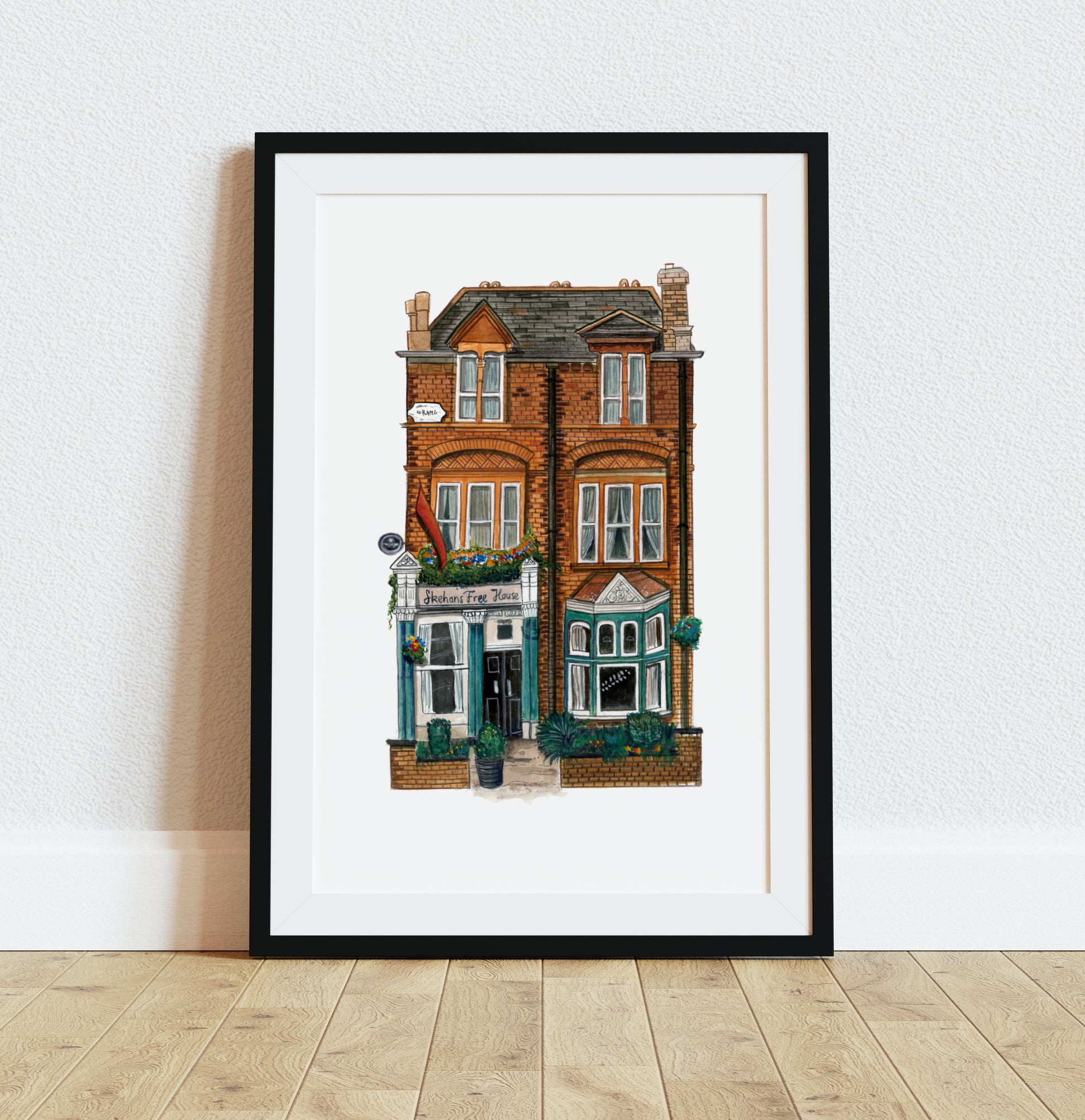 Skehans Pub art print in black frame on wooden floor against white wall