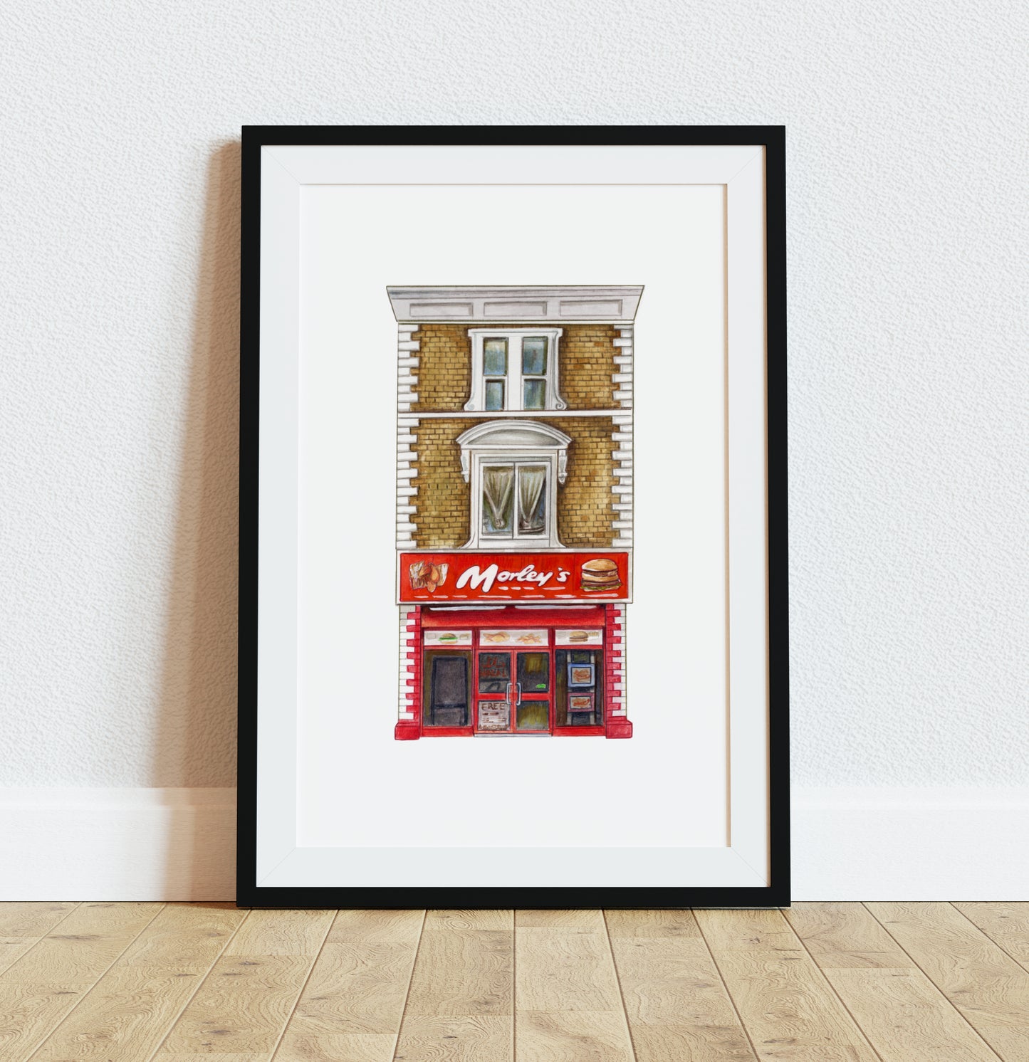 Morley’s chicken shop art print in black frame on wooden floor with white walls